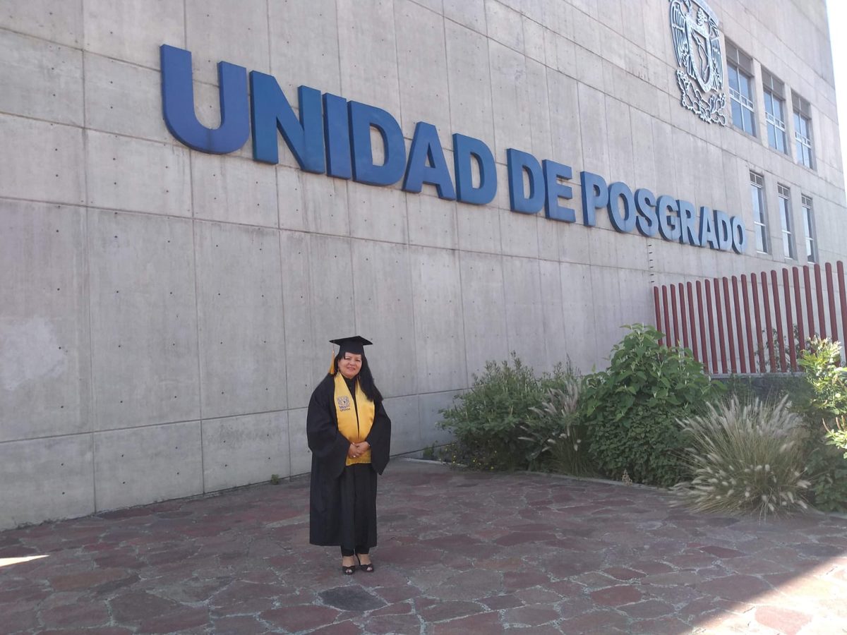Edith Méndez Romero con toga y estola de posgrado frente a la Unidad de Posgrado de la UNAM